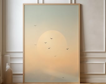 May include: A framed art print featuring a serene sunset scene. The artwork depicts a large, soft yellow sun setting behind a hazy horizon, with several small black birds in flight. The sky transitions from a pale blue to a warm orange.