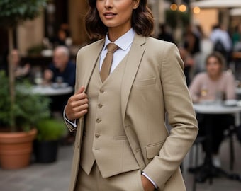 May include: A three-piece tan suit with a white collared shirt and brown tie. The suit includes a blazer, vest, and trousers. The person is standing outside, with a blurred background of a cafe.