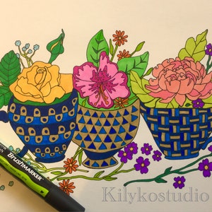 Op de afbeelding: Drie theekopjes met bloemstukken. De theekopjes zijn versierd met blauwe, gouden en witte patronen. De bloemen zijn geel, roze en perzikkleurig.