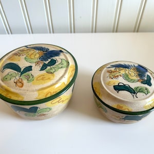 May include: Two ceramic lidded boxes with a yellow, green, and blue floral design featuring a dragon. The larger box is slightly taller than the smaller box.