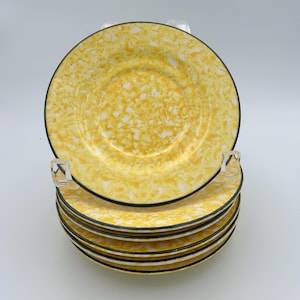May include: A stack of six round plates featuring a yellow and white marbled pattern with a thin black rim. The plates are displayed on a clear plastic stand, showing a consistent circular design across each individual piece in the set.
