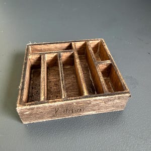 May include: A rectangular wooden organiser tray with multiple compartments of varying sizes. The dark brown wood features a visible grain and a burnt-edge finish. The word Kitchen is etched into the front side of the wooden frame.