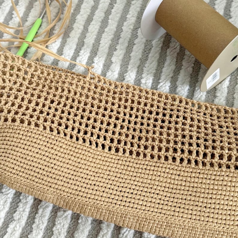 May include: A close-up of a beige crocheted bag with a woven pattern. The bag is made of a natural fiber and has a textured surface.