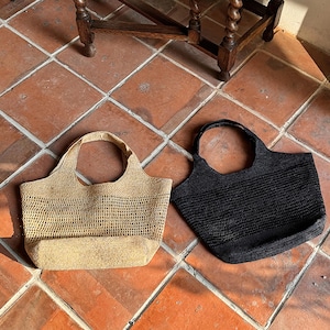 May include: Two woven tote bags, one beige and one black, with a grid pattern. The bags are sitting on a tiled floor.