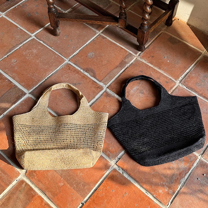 May include: Two woven tote bags, one beige and one black, with a grid pattern. The bags are sitting on a tiled floor.