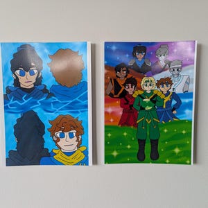 May include: Two framed art prints featuring cartoon characters. One print shows a character with blue eyes and a blue outfit, with a blue lightning background. The other print shows a group of characters in various outfits, standing on a green field.