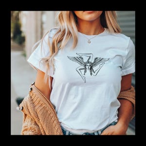 May include: White t-shirt with a black and white graphic of a winged figure with three legs.