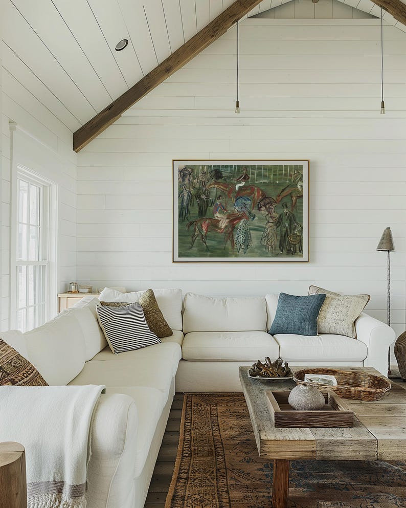 May include: A bright, airy living room with a white sectional sofa, patterned throw pillows, and a rustic wooden coffee table. A framed painting of horses hangs above the sofa. The room features a white ceiling and walls, with a wooden beam and a patterned rug.