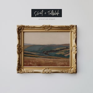 May include: A framed landscape painting with a gold ornate frame. The artwork depicts rolling hills in shades of brown, green, and blue. The text "Scout + Tallulah" and "printed and shipped" are above the frame.