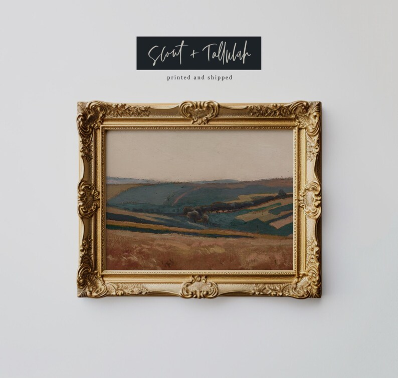 May include: A framed landscape painting with a gold ornate frame. The artwork depicts rolling hills in shades of brown, green, and blue. The text "Scout + Tallulah" and "printed and shipped" are above the frame.