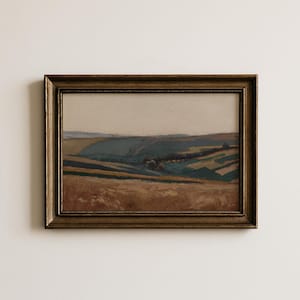 May include: A framed landscape painting with a gold-colored ornate frame. The artwork depicts rolling hills in shades of brown, green, and blue under a pale sky. The painting evokes a sense of tranquility and natural beauty.