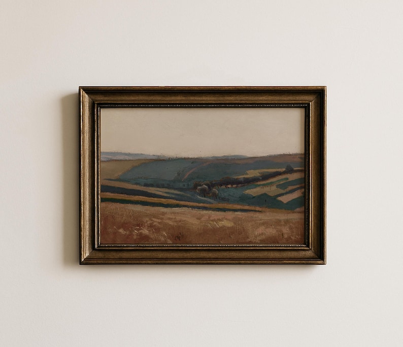 May include: A framed landscape painting with a gold-colored ornate frame. The artwork depicts rolling hills in shades of brown, green, and blue under a pale sky. The painting evokes a sense of tranquility and natural beauty.