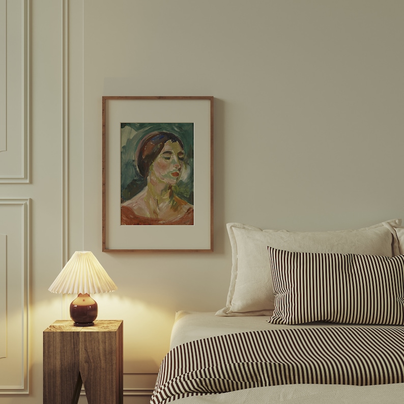 May include: A framed painting of a woman with a red and green hat, wearing a red dress, against a green background. The painting is hanging on a wall above a bed with a striped comforter.