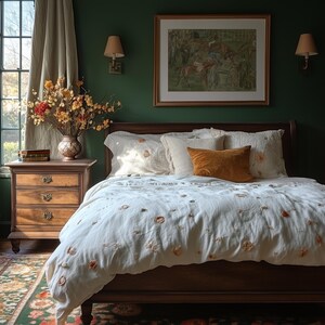 May include: A bedroom scene featuring a wooden bed with a white comforter and pillows. The comforter is adorned with floral embroidery. An orange velvet pillow adds a pop of color. A wooden nightstand with a vase of flowers and a framed artwork complete the cozy setting.