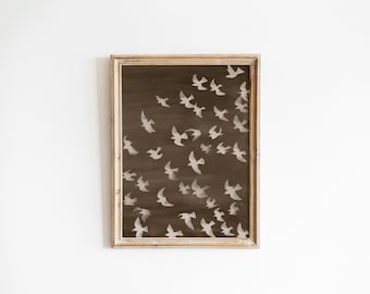 May include: A framed artwork featuring a flock of white birds against a dark brown background. The birds are depicted in flight, creating a sense of movement. The frame is a light brown color, adding a vintage touch to the piece.