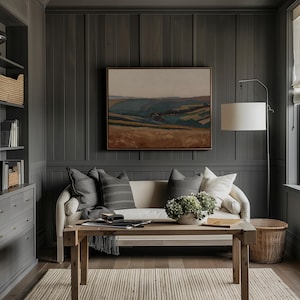 May include: A cozy living room with a neutral color palette. A cream-colored sofa is adorned with gray pillows, and a wooden coffee table holds a decorative bowl. A landscape painting hangs above the sofa, and a floor lamp provides soft lighting.