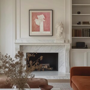 May include: A white marble fireplace with a black fireplace insert. A brown couch is in the foreground with a vase of dried flowers on a white marble coffee table. A framed abstract painting with a pink background hangs above the fireplace.