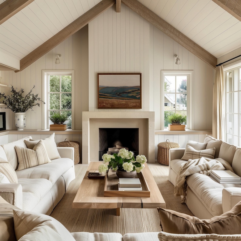 May include: A cozy living room with a neutral color palette. Features include a light wood coffee table, cream-colored sofas, a fireplace with a landscape painting, and large windows. The room is decorated with plants and woven baskets, creating a warm and inviting atmosphere.