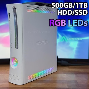 May include: White Xbox 360 console with RGB LED lights. The console has the text "XBOX 360" and the text "500GB/1TB HDD/SSD RGB LEDs". The console has a multi-colored light ring on the front and a multi-colored light strip on the top and bottom.