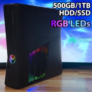 May include: Black Xbox 360 console with RGB LEDs. The console has the text "500GB/1TB HDD/SSD" and "RGB LEDs" in white and purple. The console also has the text "XBOX 360" in white.