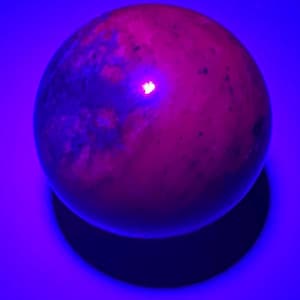 May include: A smooth, round, pink and grey sphere with a slight sheen. The sphere is illuminated by a bright, pink light, casting a shadow on a blue surface.