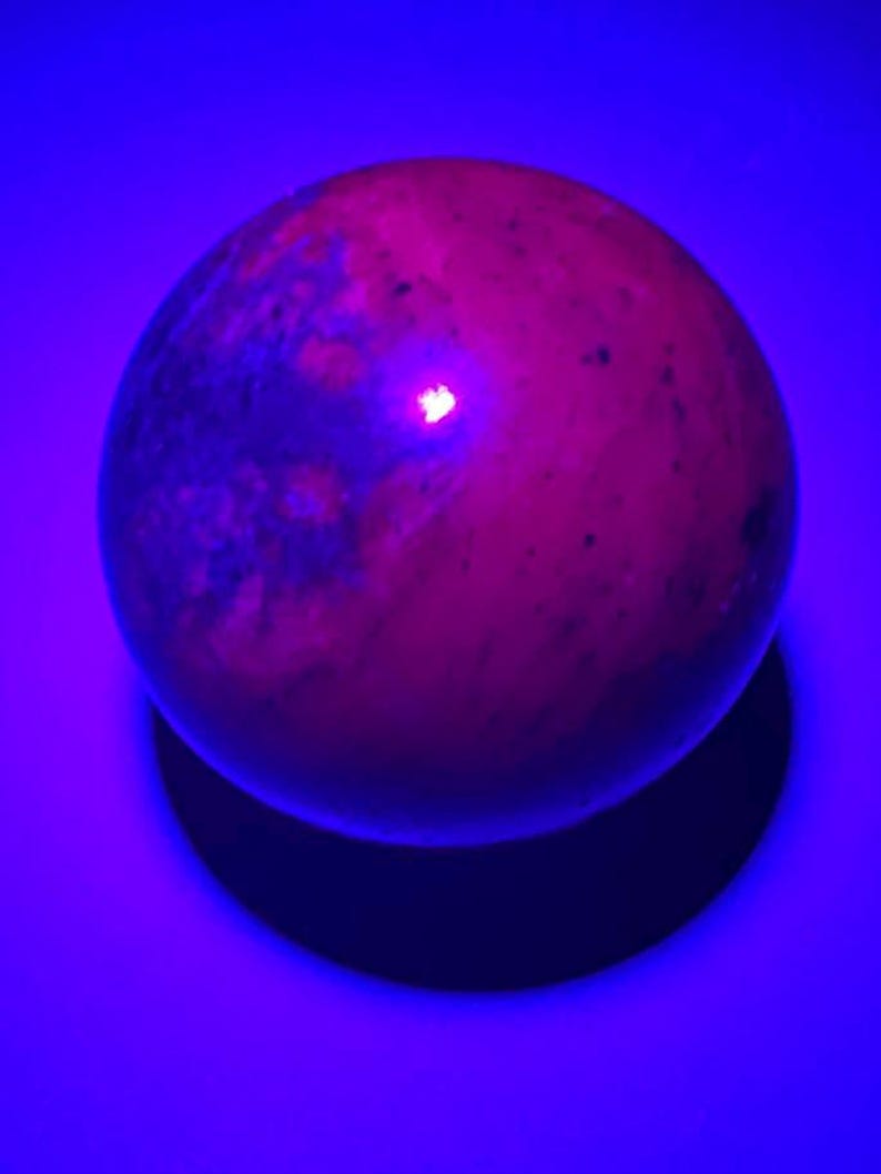 May include: A smooth, round, pink and grey sphere with a slight sheen. The sphere is illuminated by a bright, pink light, casting a shadow on a blue surface.