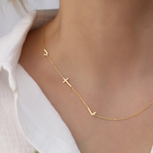 Puede incluir: Un collar de oro con una cruz y dos letras, J y L, colgando de él.