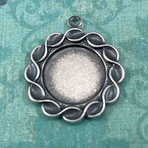 May include: A silver pendant featuring a round, smooth, blank surface encircled by a decorative, twisted, rope-like border. The pendant has a loop at the top for attaching a chain.