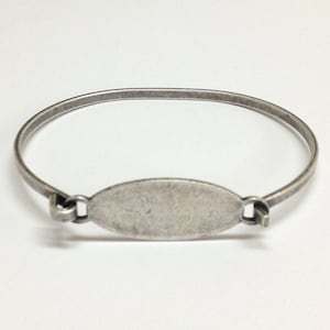 Peut inclure: Un bracelet jonc en argent avec une étiquette ovale vide. Le bracelet est ouvert et prêt à être porté.