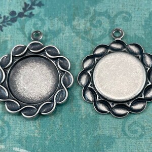 May include: Two silver-toned pendant trays with scalloped edges. The trays are round and have a smooth, slightly textured surface. They are ideal for adding a personal touch to jewellery making.