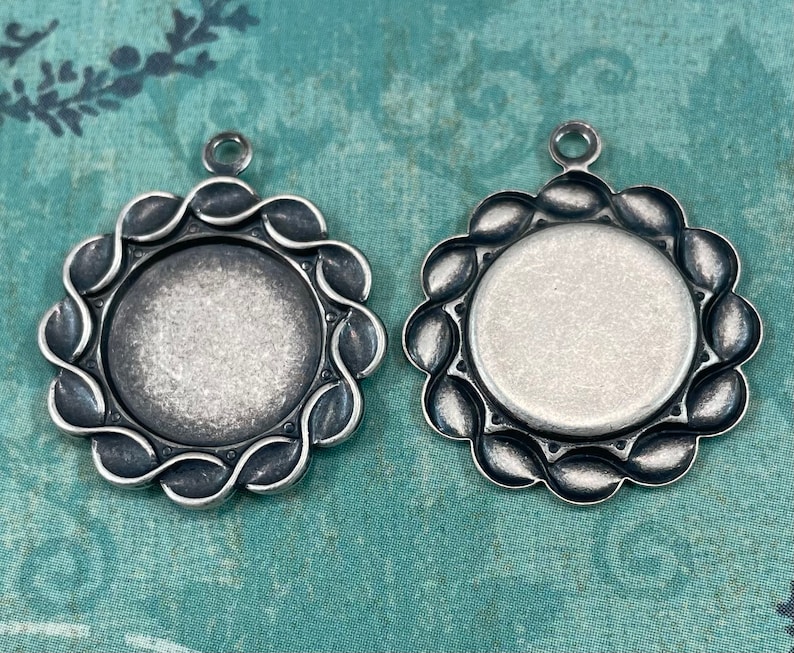 May include: Two silver-toned pendant trays with scalloped edges. The trays are round and have a smooth, slightly textured surface. They are ideal for adding a personal touch to jewellery making.
