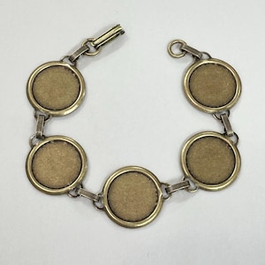 May include: A gold-toned bracelet with five round, blank, metal charms connected by a chain. The bracelet has a clasp closure.