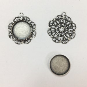May include: Three silver-toned metal pendant trays with intricate filigree designs. The trays are round and have a raised edge. The largest tray has a diameter of approximately 2 inches.