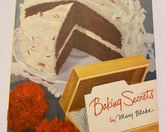 May include: A vintage cookbook titled "Baking Secrets by Mary Blake" with a photo of a frosted chocolate cake and red carnations on the cover.
