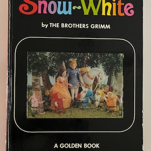 May include: A black hardcover book titled Snow-White by The Brothers Grimm, A Golden Book. The cover features a central rectangular inset illustration of Snow White, a prince, a white horse, and seven dwarfs in a forest setting.