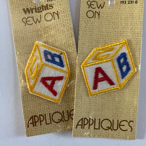 May include: Two packages of Wrights Sew On appliques. Each package contains a single applique of a yellow, red, and blue block with a letter on each side. The first package has the letter A and the second package has the letter B. The packages are both $1.00.