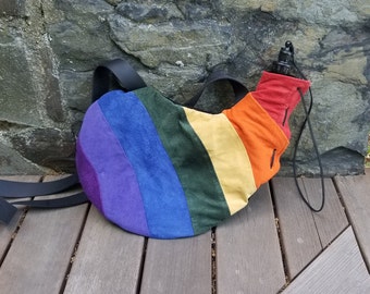Puede incluir: Una bolsa de tela con rayas de arcoíris con una correa negra y una botella de agua negra en su interior. La bolsa está hecha de un material suave, similar al ante.