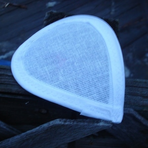 May include: A white, triangular-shaped fascinator base featuring a woven, mesh-like fabric texture. The piece has a smooth, solid white border along its curved edges, providing a clean, structured outline to the overall form of the accessory.