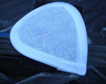 Puede incluir: Una base de tocado triangular de color blanco con una textura de tela tejida similar a una malla. La pieza presenta un borde blanco liso y sólido a lo largo de sus lados curvos, proporcionando un contorno limpio y estructurado al accesorio.