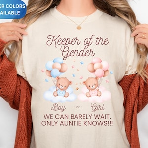 May include: Cream-colored t-shirt with the text "Keeper of the Gender." The shirt features illustrations of teddy bears on clouds with balloons, in pink and blue. The text "Boy or Girl" is also present.