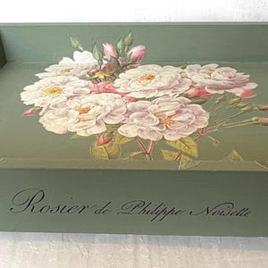 Puede incluir: Una bandeja de servicio rectangular de color verde salvia con asas recortadas y pies pequeños. La base interior presenta una ilustración floral de rosas blancas y rosas. El frente muestra el texto cursivo negro, Rosier de Philippe Noisette.