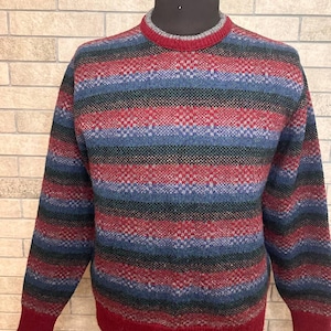 May include: A multi-colored sweater with a round neck and long sleeves. The sweater features horizontal stripes in red, blue, green, and gray. The cuffs and hem are a solid red color. The sweater is displayed on a mannequin.
