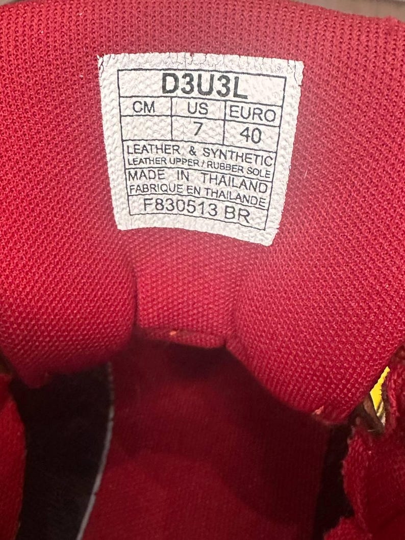 May include: Close-up of the inside of a red shoe. A white tag displays size information: UK 7, Euro 40. The shoe is made with leather and synthetic materials, with a rubber sole. The tag also indicates the shoe was made in Thailand.