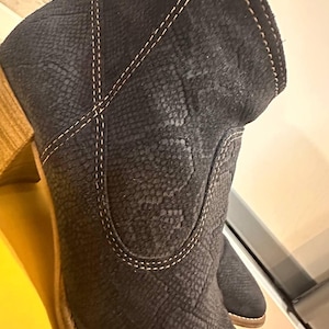 Op de afbeelding: Donker marineblauwe enkellaarsjes met een textuur, slangenleerachtig patroon. De laarzen hebben een gestapelde houten hak en witte stiksels. Het ontwerp omvat een spitse neus en een licht schuine bovenkant.