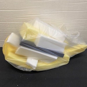 May include: A clear plastic bag filled with various foam pieces. The foam pieces are in shades of white, yellow, and black. The bag is partially open, revealing the contents.