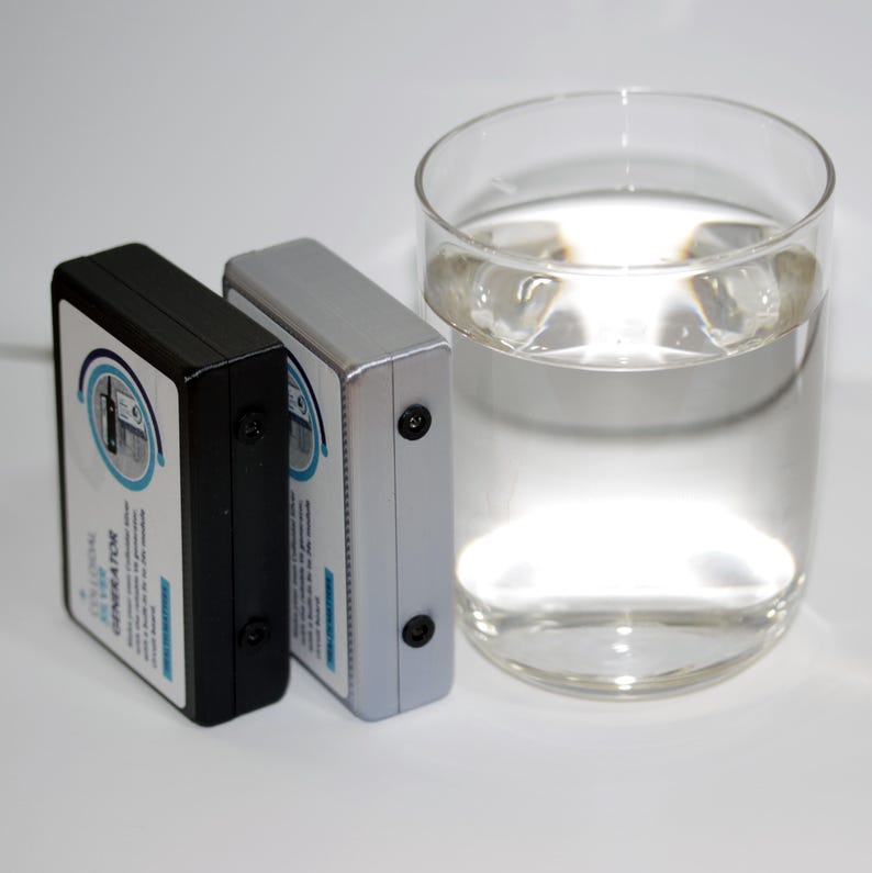 May include: Two rectangular devices, one black and one silver, are positioned next to a clear glass of water. The devices have a label with text and a circular design. The glass is filled with clear liquid and ice cubes.