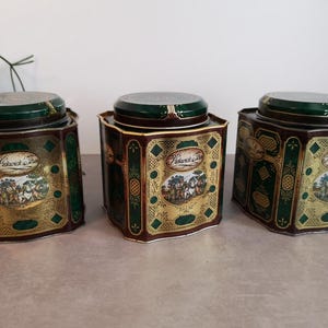 Op de afbeelding: Drie vintage groene, gouden en bruine metalen theeblikken met een jachtscène ontwerp en de tekst "Peacock & Tree".