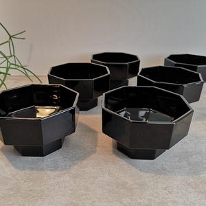Peut inclure: Six bols noirs de forme géométrique sont disposés sur une surface grise. Les bols ont une finition brillante et un design unique à multiples facettes. Ces bols sont probablement destinés au service ou à l'exposition.