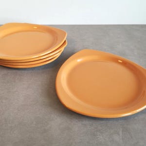 Op de afbeelding: Een set van vijf effen oranje borden met een gladde, glanzende afwerking en een opvallende driehoekige vorm met afgeronde hoeken. De borden hebben een licht opstaande rand en een plat midden, uitgevoerd in een uniforme, levendige oranje kleur.