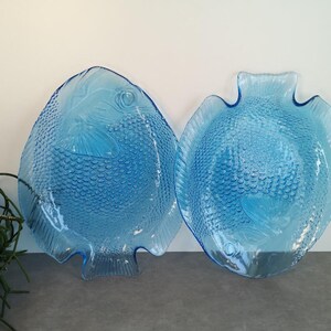 Op de afbeelding: Twee blauwe glazen visvormige serveerschalen. De schalen zijn getextureerd om op vissen schubben te lijken.